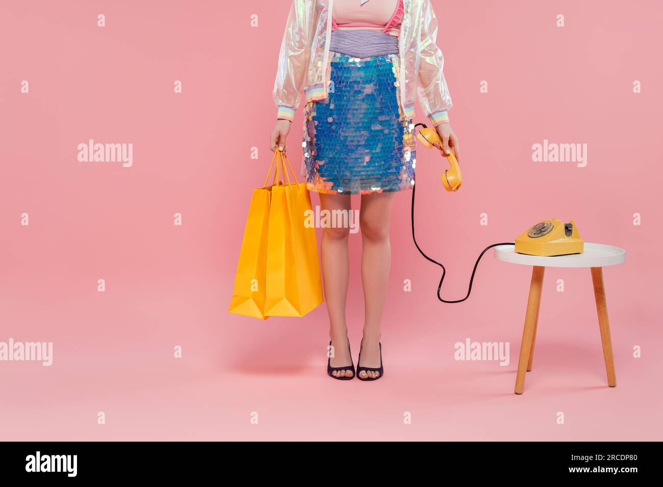 Konzeptionelle Fotografie, freigestellte Ansicht einer jungen Frau mit Einkaufstaschen und Retro-Telefon in der Hand, auf rosa Hintergrund stehend, Telefonanruf, Vinta Stockfoto
