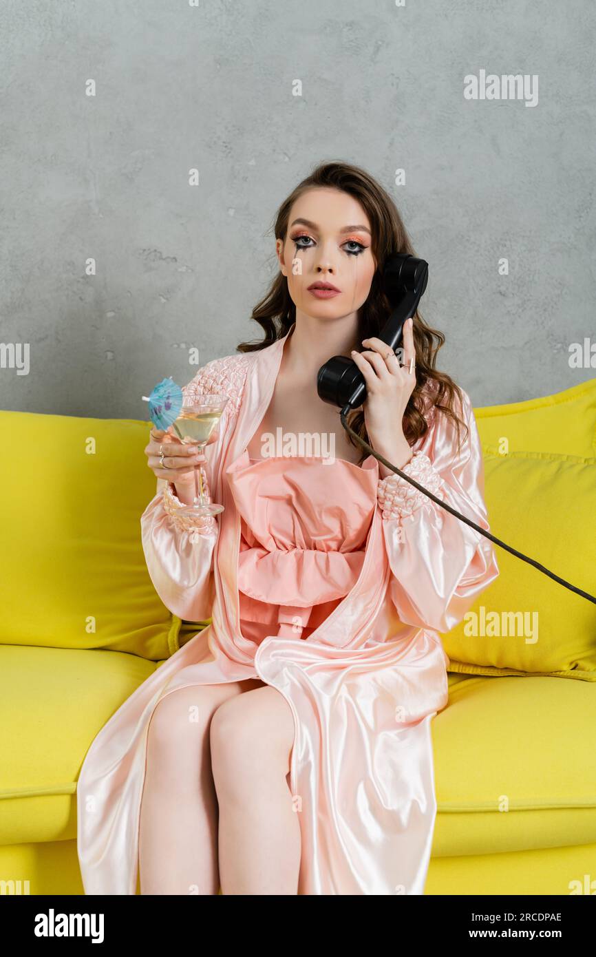 Emotionaler Stress, traurige Frau mit verwischter Mascara, die auf der gelben Couch sitzt, Hausfrau mit weinenden Augen, die auf einem Retro-Telefon spricht, sich einsam fühlt und deprimiert Stockfoto