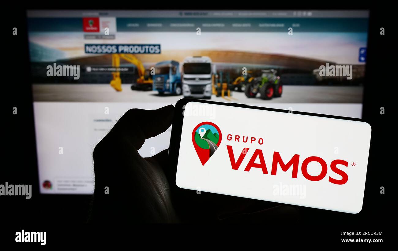 Person, die ein Mobiltelefon mit dem Logo der brasilianischen Lkw-Vermietungsfirma Grupo Vamos auf dem Bildschirm vor der geschäftlichen Webseite hält. Konzentrieren Sie sich auf das Display des Telefons. Stockfoto
