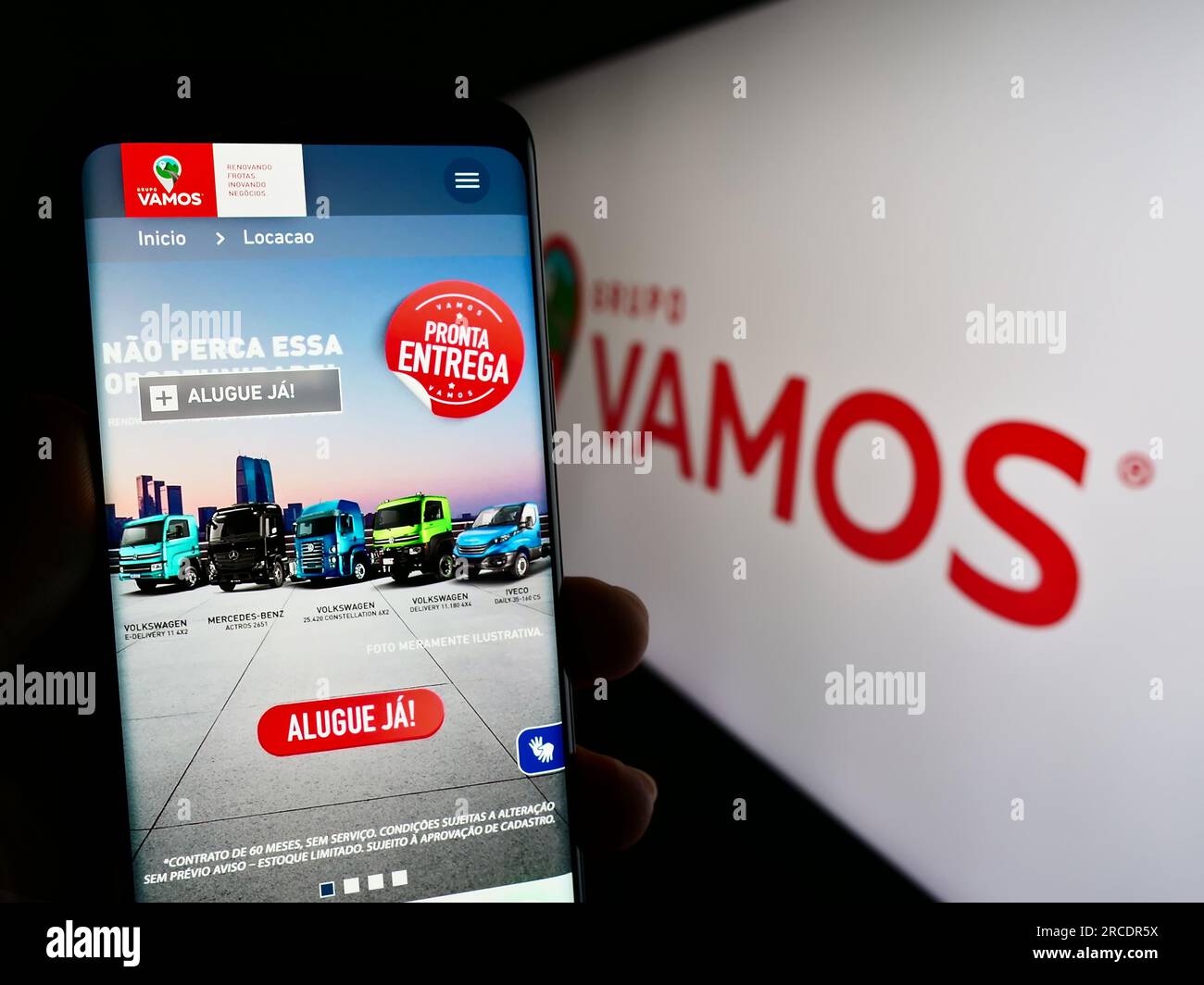 Person, die ein Mobiltelefon mit einer Webseite des brasilianischen Lkw-Vermietungsunternehmens Grupo Vamos auf dem Bildschirm vor dem Logo hält. Konzentrieren Sie sich auf die Mitte des Telefondisplays. Stockfoto