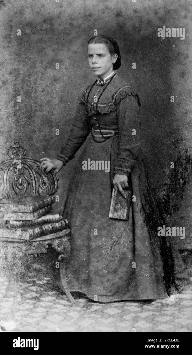 Ein langes Porträt einer jungen Dame in einem langen Kleid, deren Hand auf einem Stuhl ruht, der mehrere Bücher mit Lederbindung enthält. Originalfotograf unbekannt. Aus einer Sammlung viktorianischer Carte de Visite Fotografien aus den 1890er Jahren. Carte de visite ist ein französischer Begriff, der auf Englisch als „Visitenkarte“ bezeichnet wird. Normalerweise wurde ein Fotodruck aus Albumen von etwa 54 x 89 mm auf einer etwas größeren Karte angebracht. In einigen Fällen haben die Verwüstungen der Zeit ihren Tribut gefordert. Stockfoto
