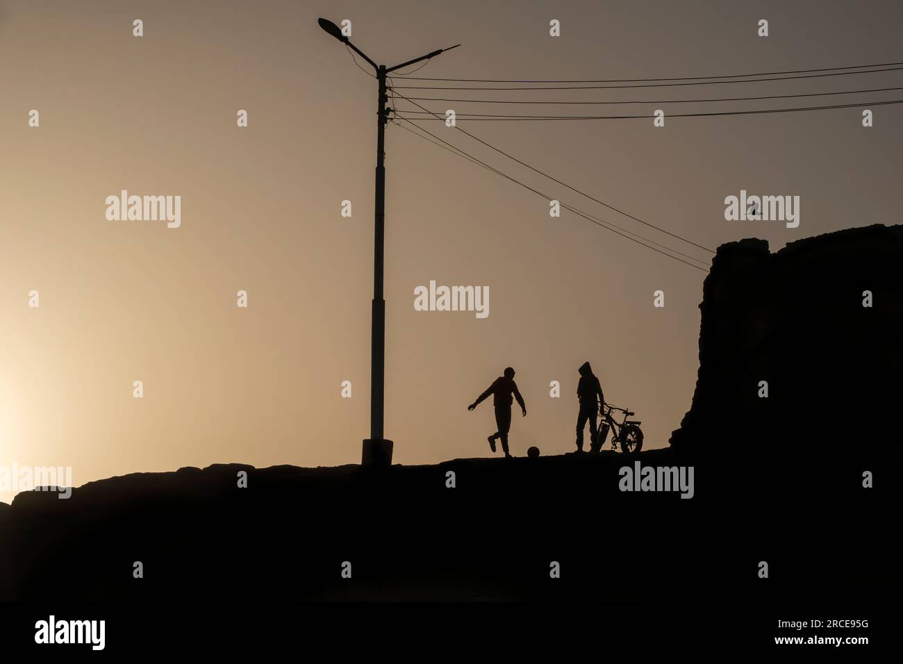 Zwei ägyptische Straßenjungen mit Fußball und Fahrrad in Silhouette Stockfoto