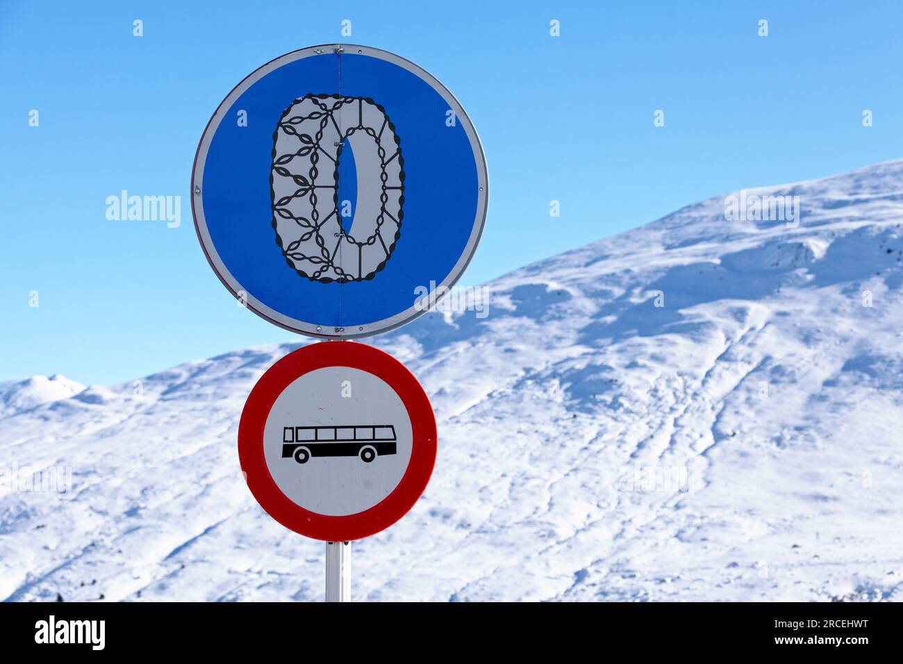 Ein Schild mit Schneeketten ist erforderlich über einem Busverbot-Schild vor einem schneebedeckten Berg in den Pyrenäen. Stockfoto