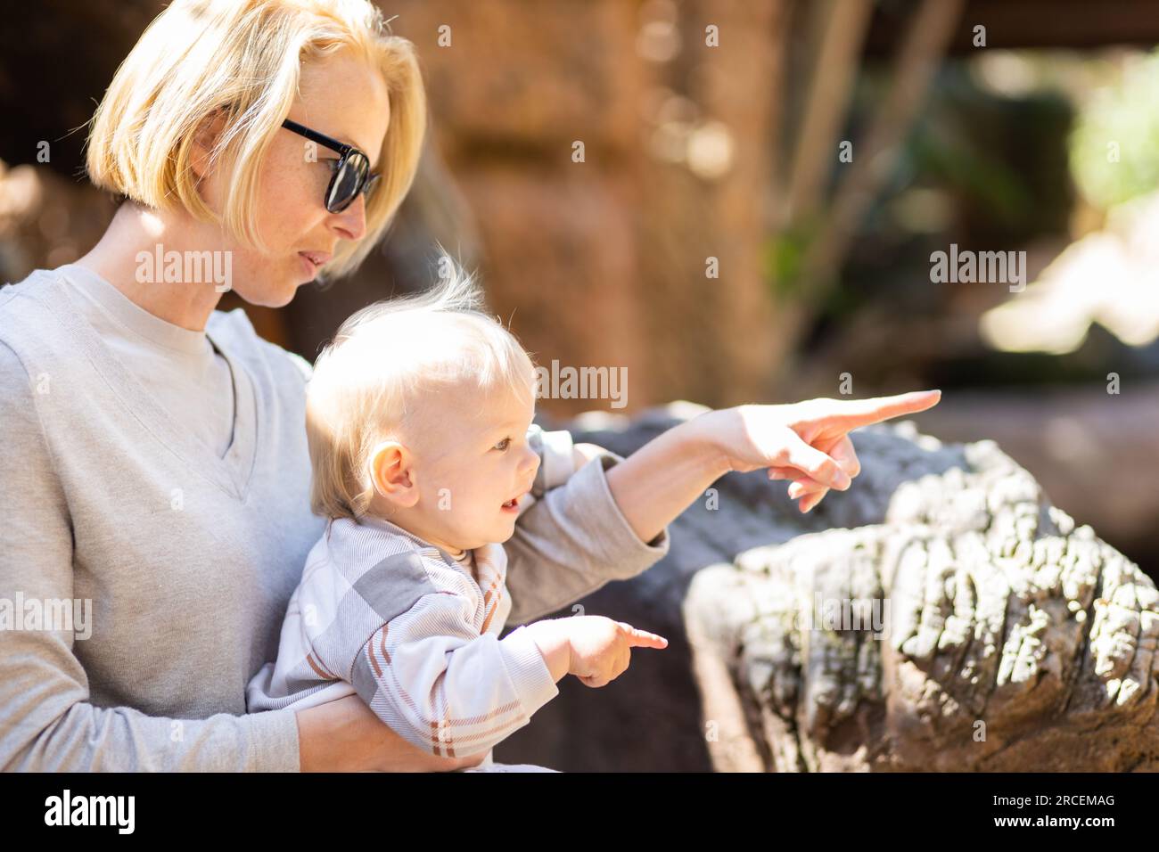 Weiße blonde Mutter, die ihr Baby im Schoß hält und Krokodile im Zoo sieht. Glückliche Familie, die Spaß mit dem Tier Safari Park auf wa hat Stockfoto