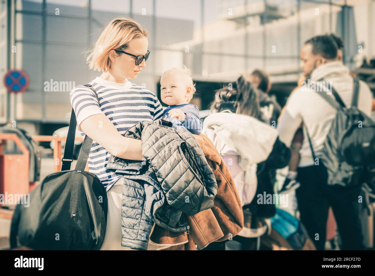 Der Mutter, die mit seinem kleinen Jungen reist. Mutter hielt Reisetasche und ihr kleines Kind, während sie sich vor dem Flughafen in der Schlange für den Bus anstellte Stockfoto