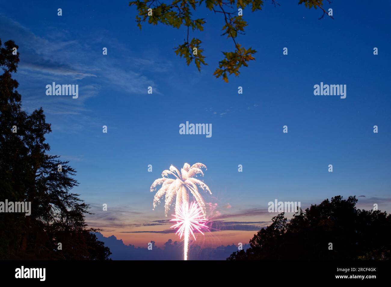 Feuerwerk in der Ferne, das in der frühen Nacht nach oben in den Sternenhimmel geht, mit Sonnenuntergang hinter den Wolken vom Regensturm auf der 4. o Stockfoto