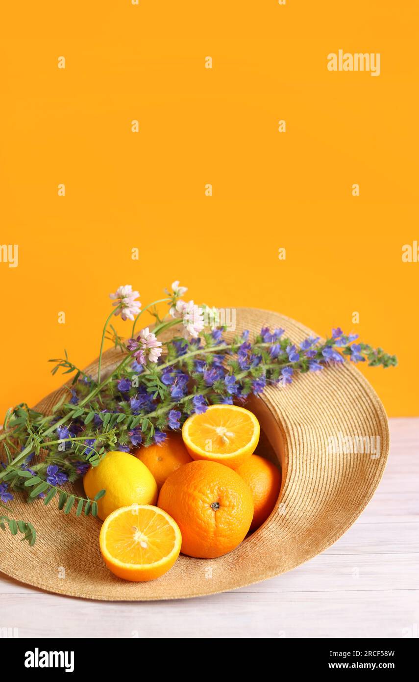 Reife, saftige Orangen in einem Sommerhut, Wildblumen. Sommerfrüchte auf hellem orangefarbenem Hintergrund. Zitrusfrüchte. Lebensmittel mit vielen Vitaminen Stockfoto