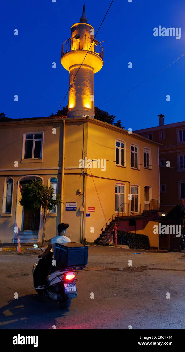Ablieferant auf einem Motorrad in der Nacht auf einer Straße in Istanbul Türkei mit einem Gebäude und einem Minarett dahinter. Stockfoto