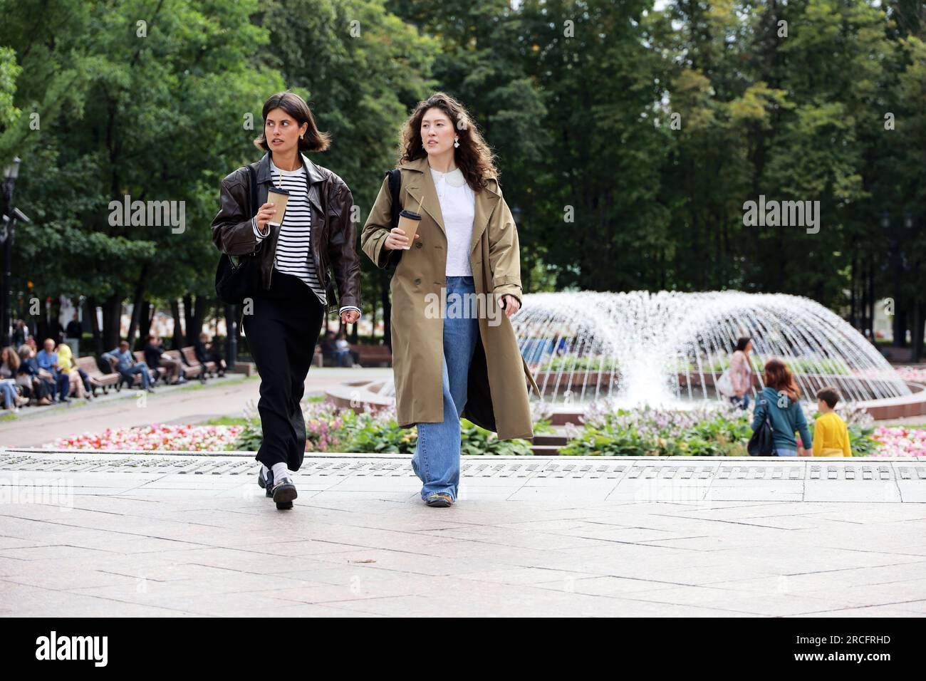 Zwei junge Frauen, die auf einer Straße spazieren gehen, mit Brunnen im Hintergrund Stockfoto