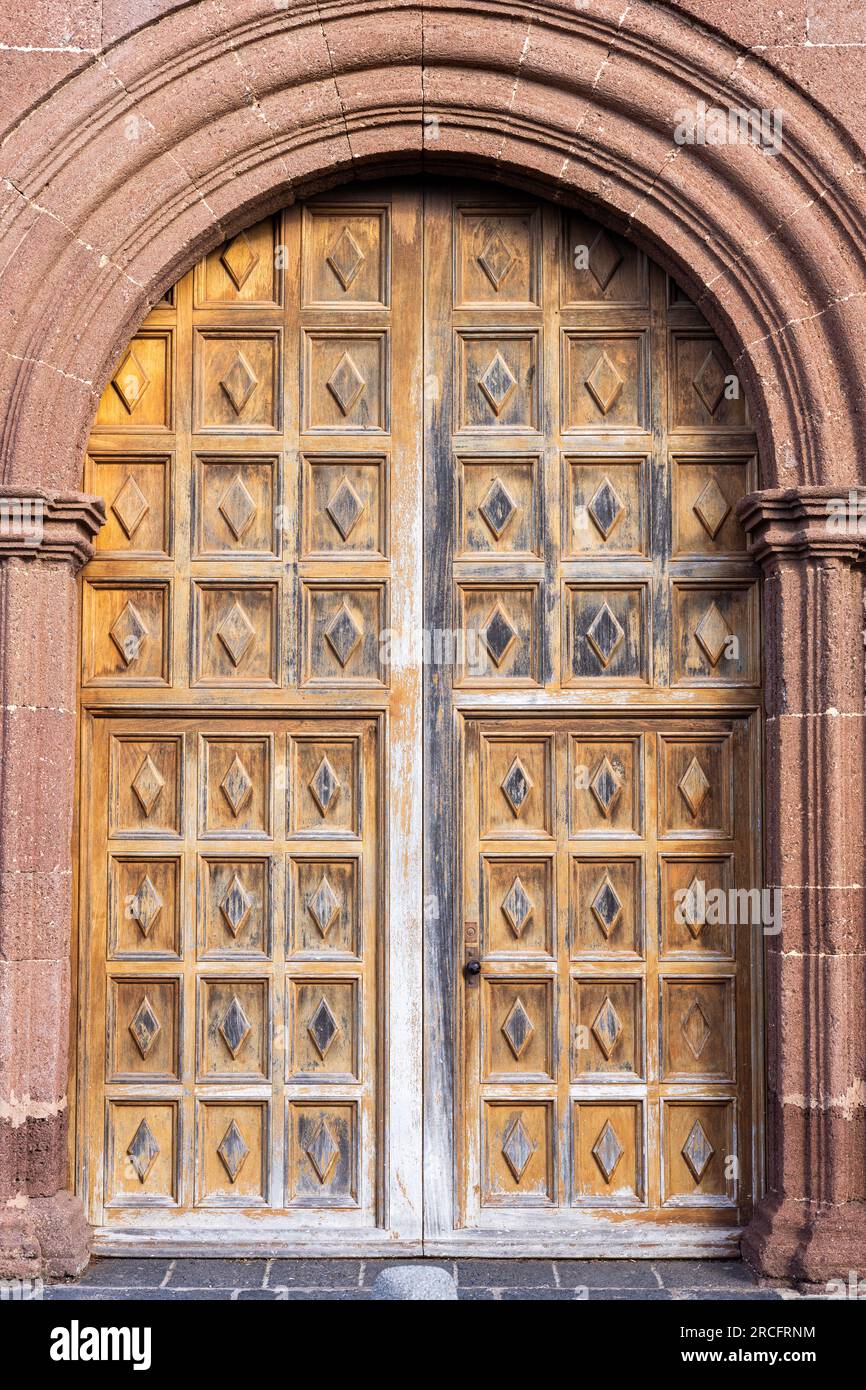 Große, wunderschöne kunstvoll verzierte Holztür, eingerahmt von einem dekorierten Steinbogen. Eintritt zu iglesia de nuestra senora de guadalupe, Teguise, Lanzarote, Kanarische Inseln Stockfoto