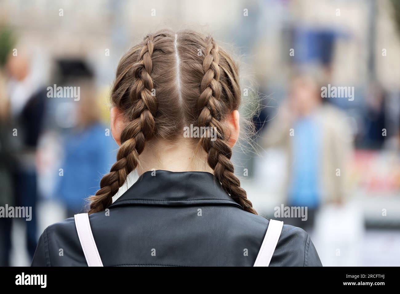 Ein Mädchen mit geflochtenen Zöpfen, das eine Lederjacke auf der Straße trägt. Weibliche Frisur und Mode in der Stadt Stockfoto