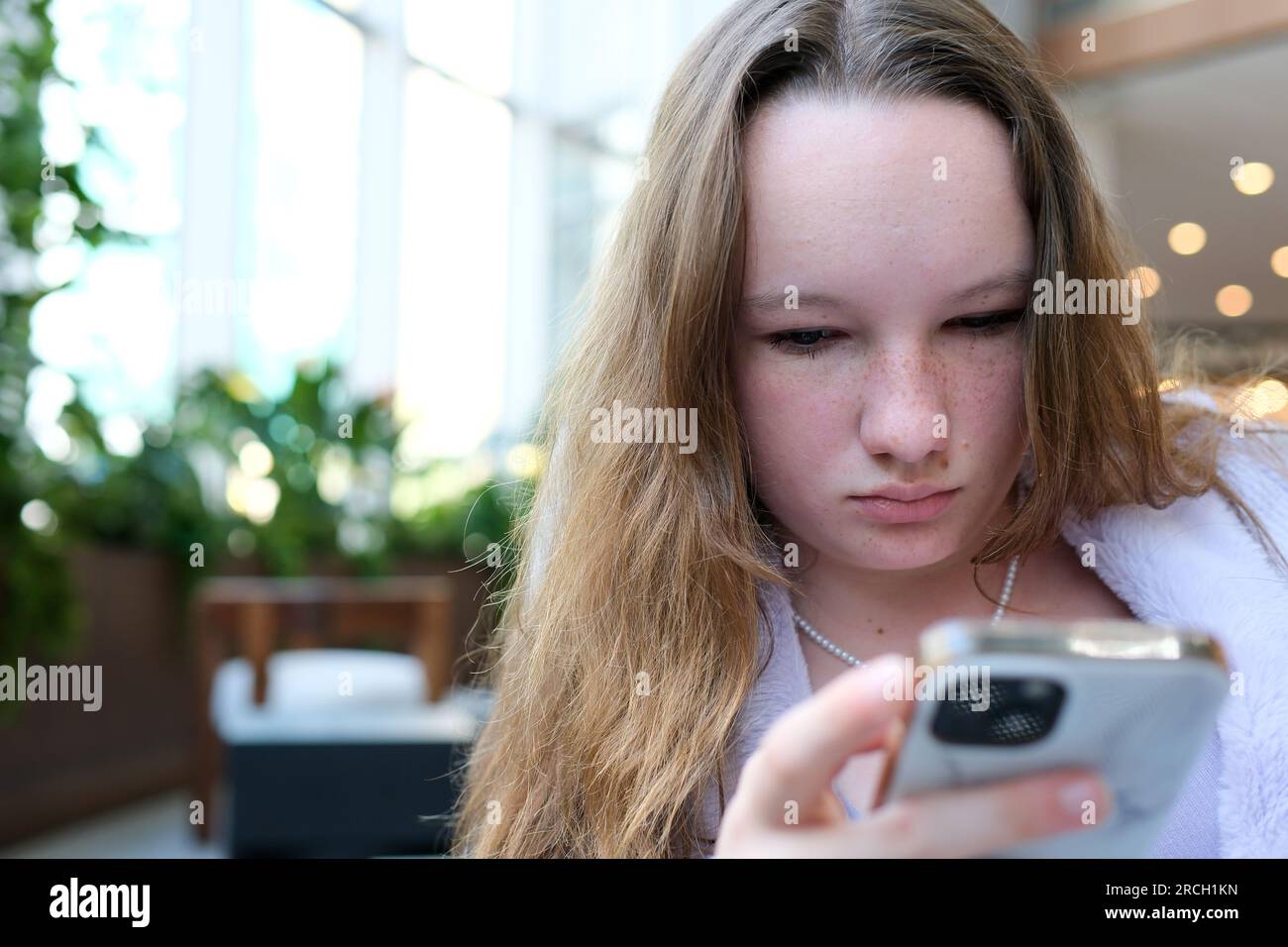 Ein junges Mädchen mit Sommersprossen eine europäische Frau sitzt mit einem Telefon in der Hand in der Lobby eines Hotels. Um nach Geolokalisierung zu suchen, buchen Sie ein Zimmer zum Ausruhen und erwarten Sie eine junge junge Person mit schönen Haaren Stockfoto