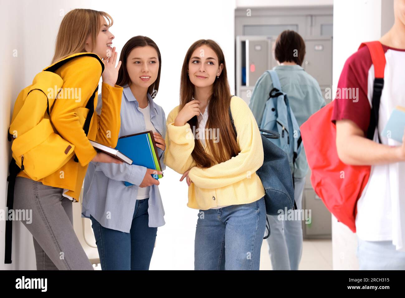 Teenager-Mädchen, die in der Schule über Klassenkameraden reden Stockfoto