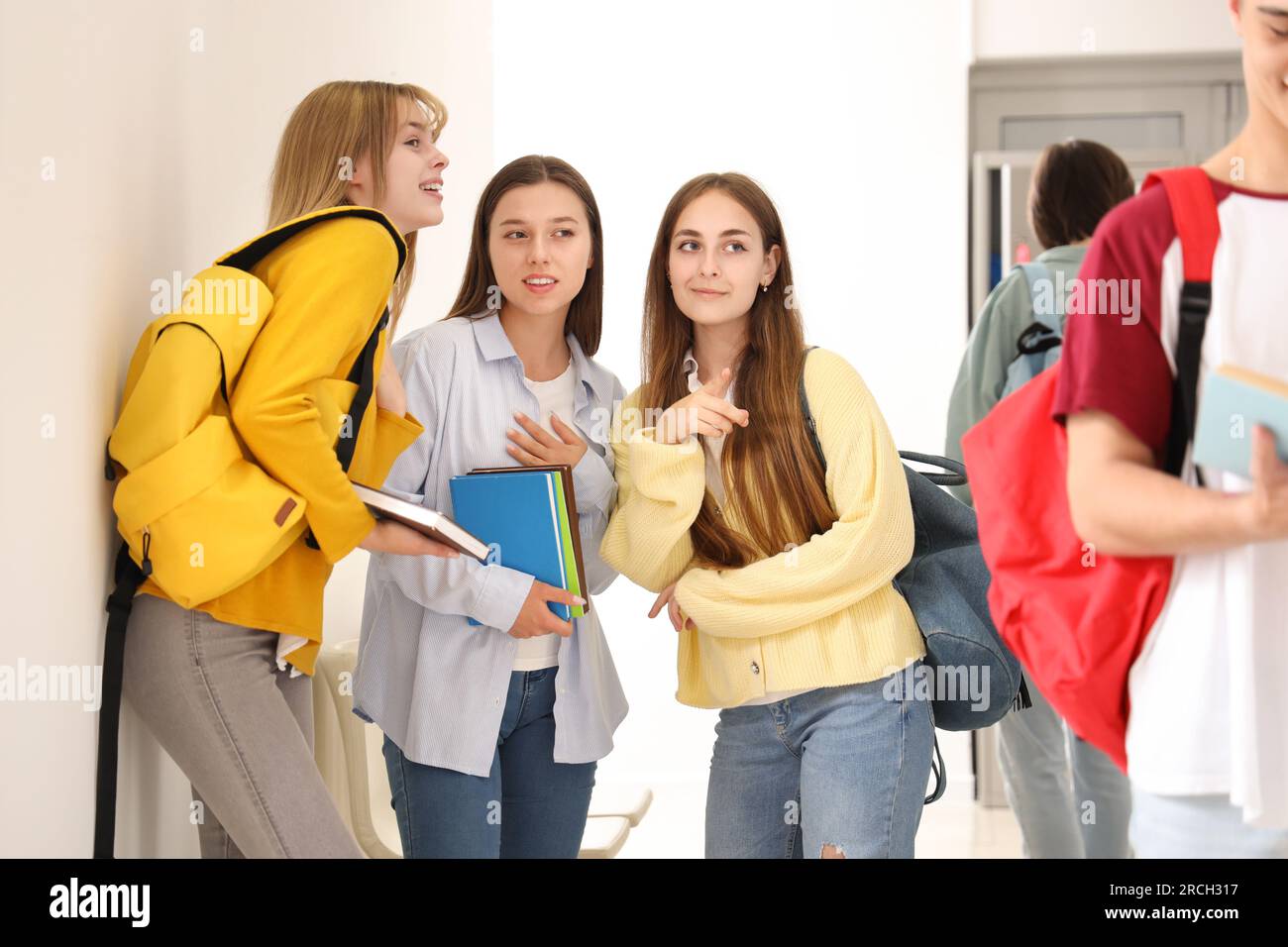 Teenager-Mädchen, die in der Schule über Klassenkameraden reden Stockfoto