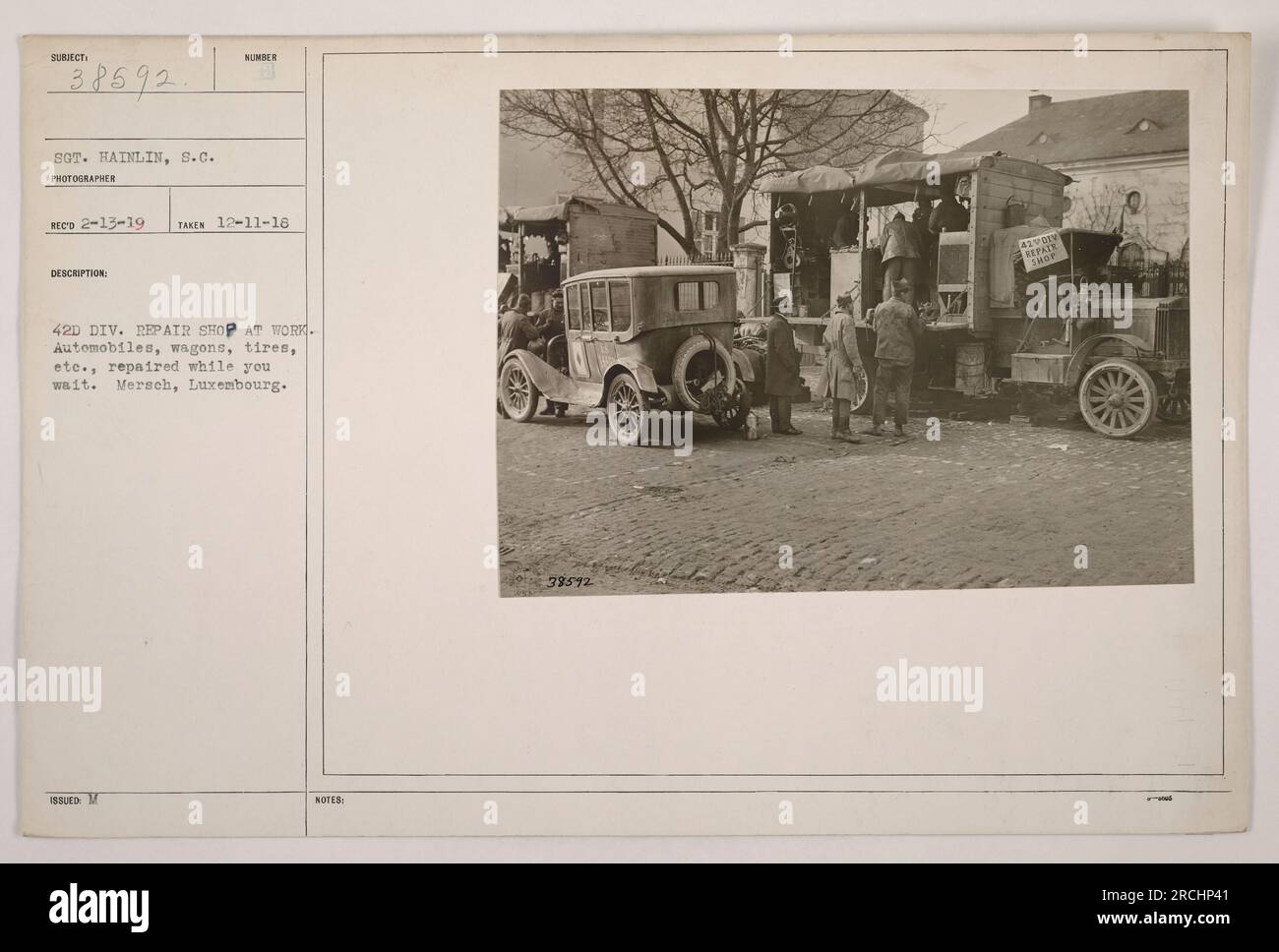 Soldaten aus der 42. Division Reparaturwerkstatt arbeiten an verschiedenen Fahrzeugen, einschließlich Autos, Wagen und Reifen, in Mersch, Luxemburg. Das Foto, das am 11. Dezember 1918 aufgenommen wurde, zeigt ihr Engagement für die schnelle Bereitstellung von Reparaturservices. Sergeant Hainlin hat diese Szene im Ersten Weltkrieg aufgenommen. Stockfoto