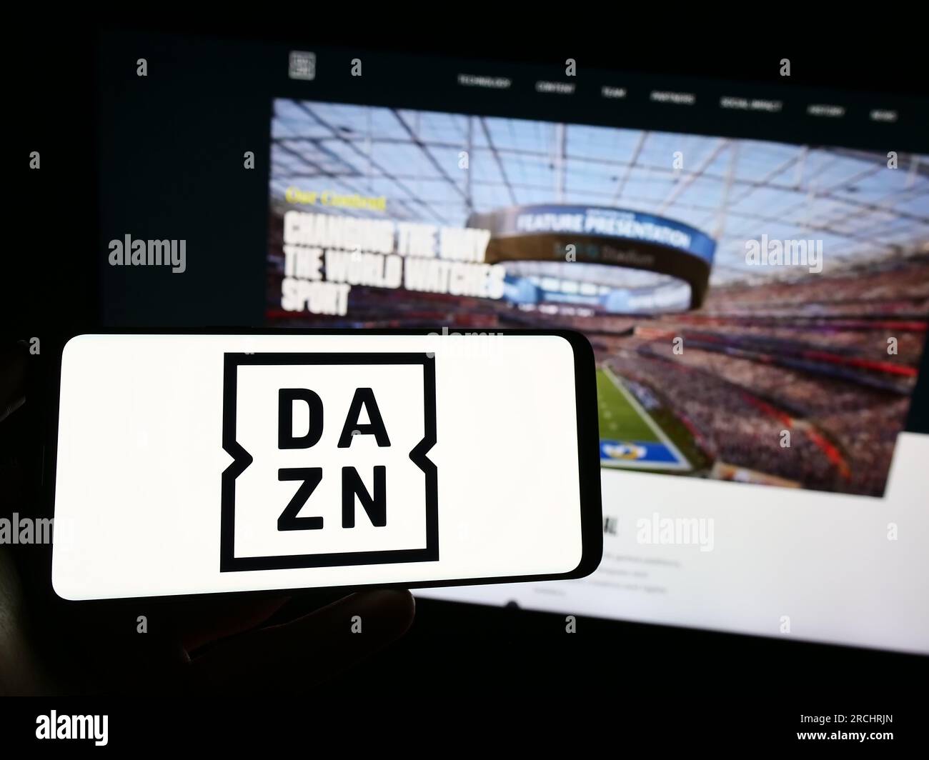 Person, die ein Mobiltelefon mit dem Logo des britischen Sportmedienunternehmens DAZN Group Limited auf dem Bildschirm vor der Webseite hält. Konzentrieren Sie sich auf das Display des Telefons. Stockfoto