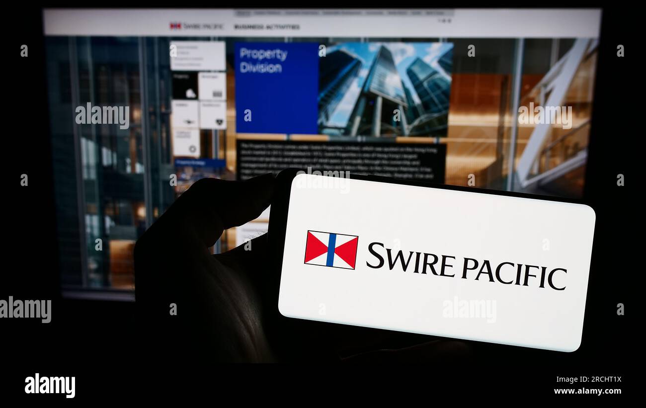 Person, die ein Mobiltelefon mit dem Logo des asiatischen Unternehmens Swire Pacific Limited auf dem Bildschirm vor der geschäftlichen Webseite hält. Konzentrieren Sie sich auf das Display des Telefons. Stockfoto