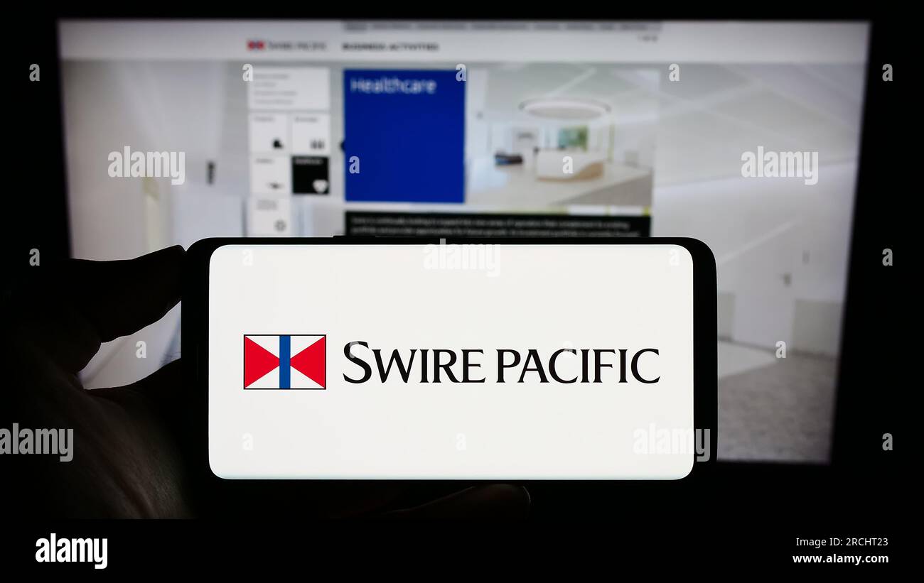 Person, die ein Mobiltelefon mit dem Logo des asiatischen Unternehmens Swire Pacific Limited auf dem Bildschirm vor der geschäftlichen Webseite hält. Konzentrieren Sie sich auf das Display des Telefons. Stockfoto