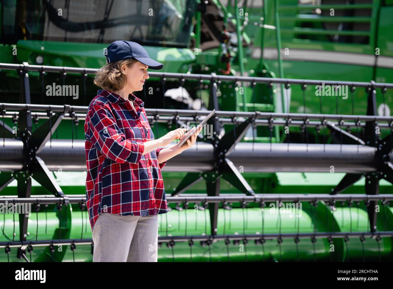 Landwirtin mit digitalem Tablet vor dem Hintergrund der Erntemaschine. Konzept der intelligenten Landwirtschaft Stockfoto