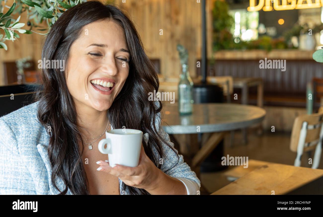Nahaufnahme einer fröhlichen Frau, die lächelt, während sie eine Tasse Kaffee in einem Café trinkt. Stockfoto