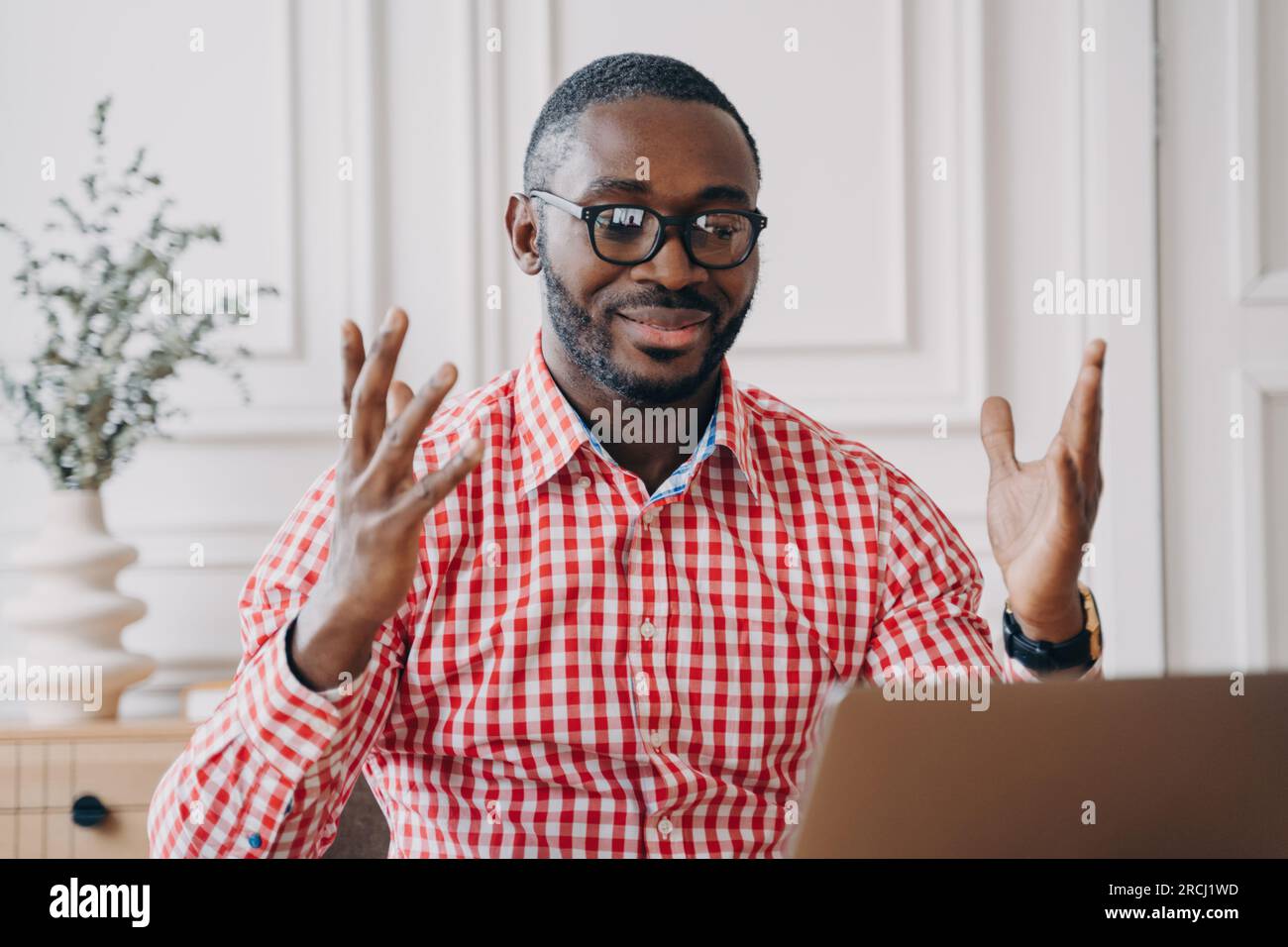 Ein ekstatischer schwarzer Mann mit Brille, der Nachrichten über Laptops liest, feiert den Erfolg des Büros; ein freudiger afrikanischer Mitarbeiter. Stockfoto