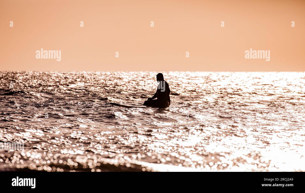 Silhouette einer Person, die auf einem Surfbrett auf dem Ozean saß. Der Himmel ist klar und wartet auf eine Welle Stockfoto