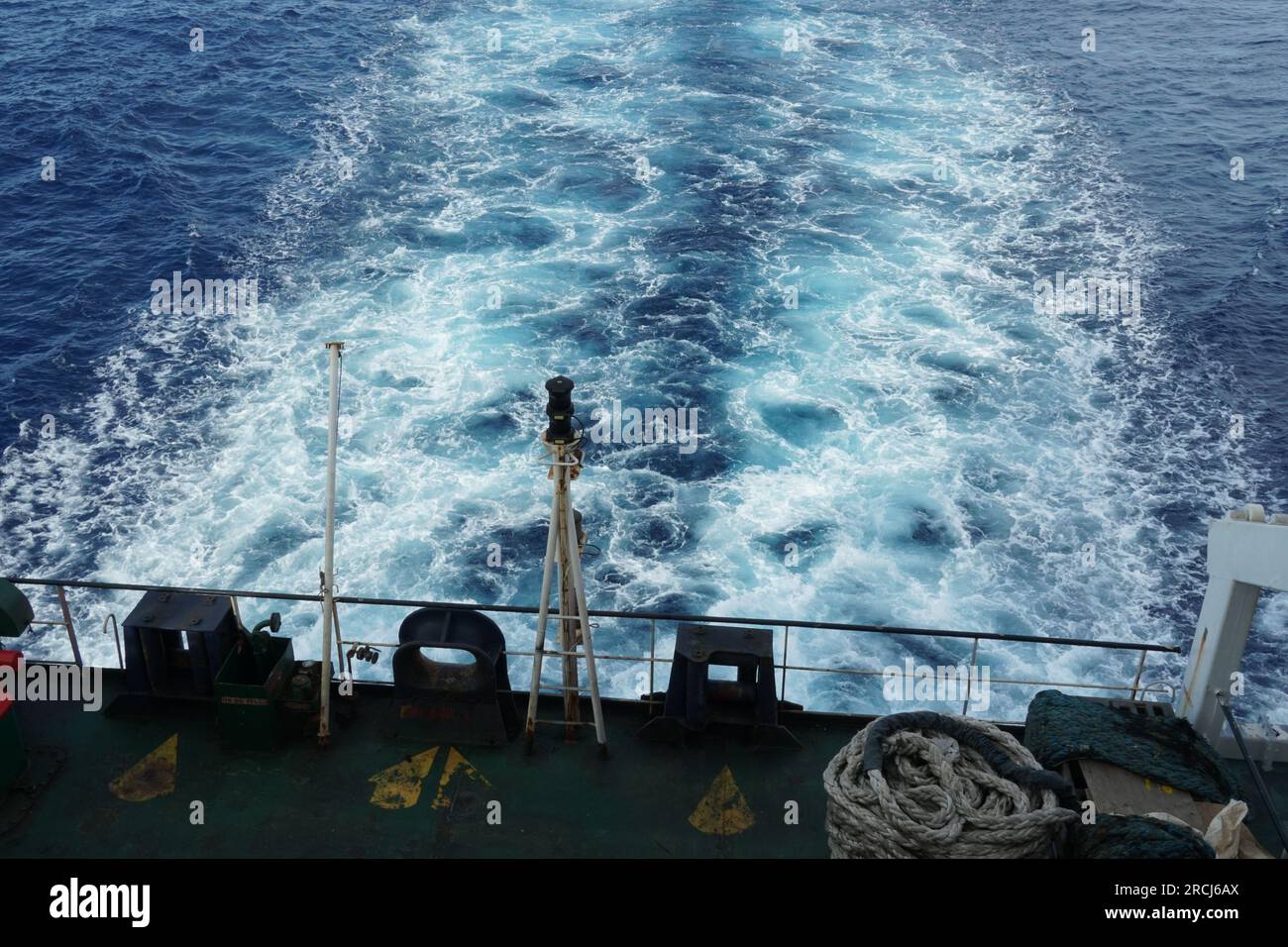 Hinter dem Schiff befindet sich Kielwasser, das von der Achterstation aus beobachtet wird, wobei das Frachtschiff im Stehlicht durch den ruhigen Ozean fährt. Stockfoto