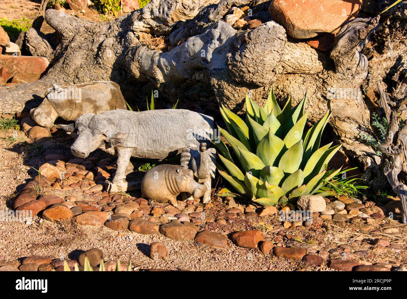 Gartendesign in afrika mit Tierskulpturen aus Holz, Nilpferden, Büffeln, Vögeln auf einem Felsbett und Aloe-Vera-Pflanzen Stockfoto
