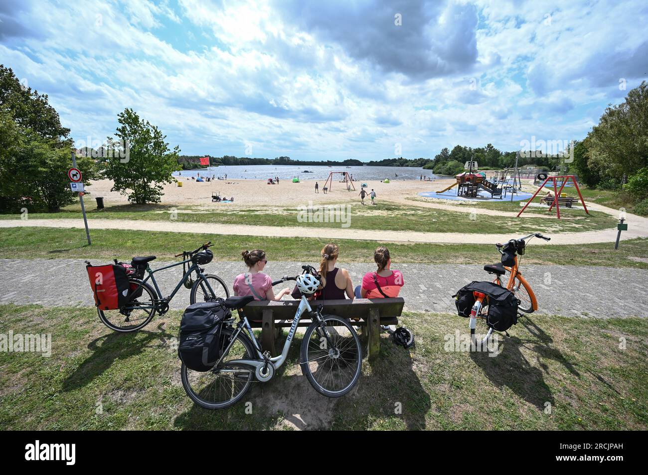 Timmel, Deutschland. 15. Juli 2023. Fahrradtouristen machen eine kurze Pause am Badesee und genießen das Wetter. Wochenendurlauber und Touristen haben sich am Samstag an den Küsten und Binnengewässern nach Abkühlung gesehnt. Mit den individuellen Duschen um 12 Uhr kündigte sich eine Kaltfront nach deutschem Wetterdienst (DWD) an, die die heiße Luft um 30 Grad verdrängen sollte. Sonntags erwartete ein Meteorologe etwa 23 Grad in Ostfriesien, etwa 27 Grad in Hannover. Kredit: Lars Penning/dpa/Alamy Live News Stockfoto