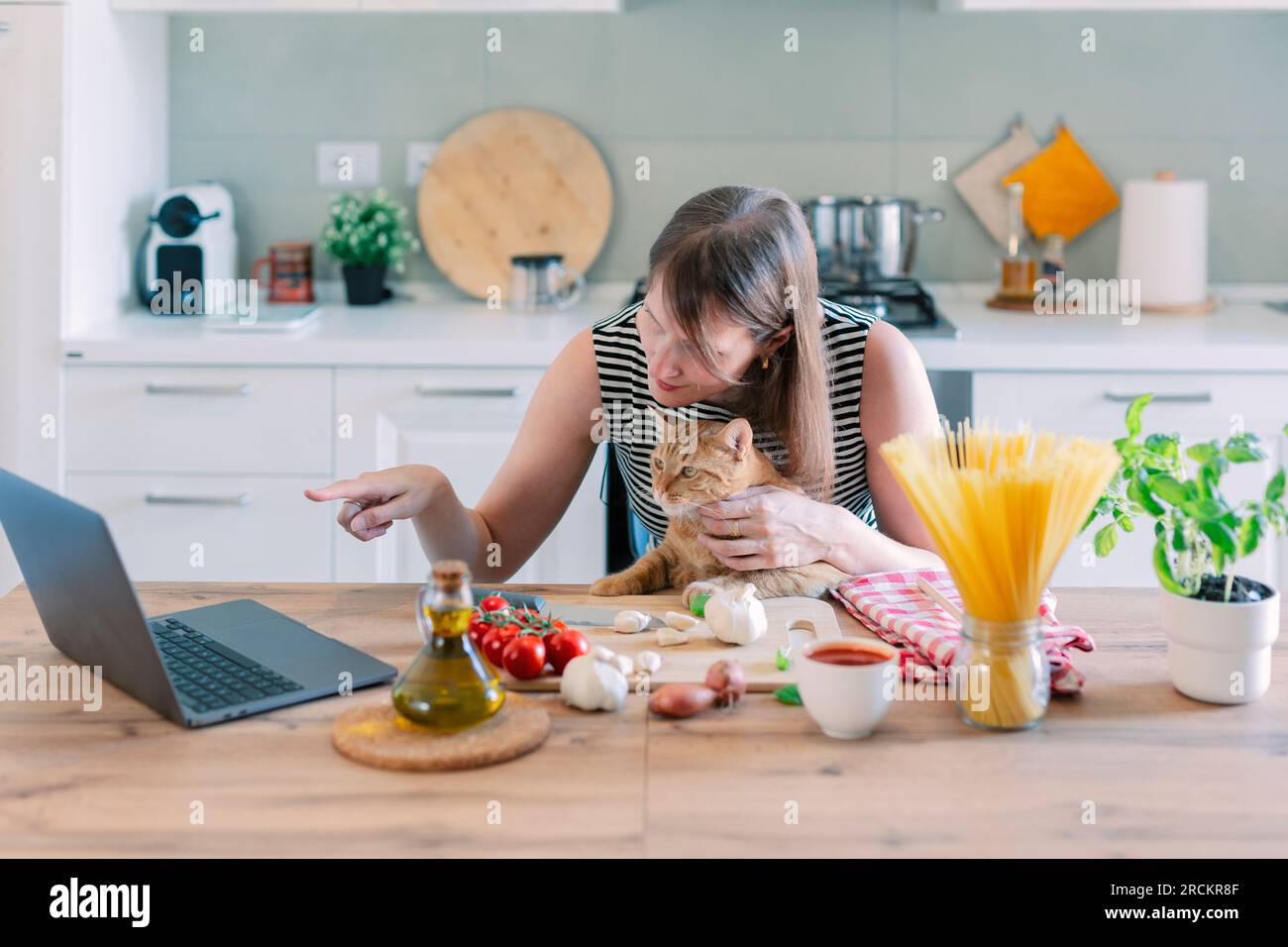 Die Katze und ihr Besitzer in Schürzen kochen gemeinsam in der heimischen Küche. Hauskatze beobachtet, wie das Mädchen das Futter salzt. Stockfoto
