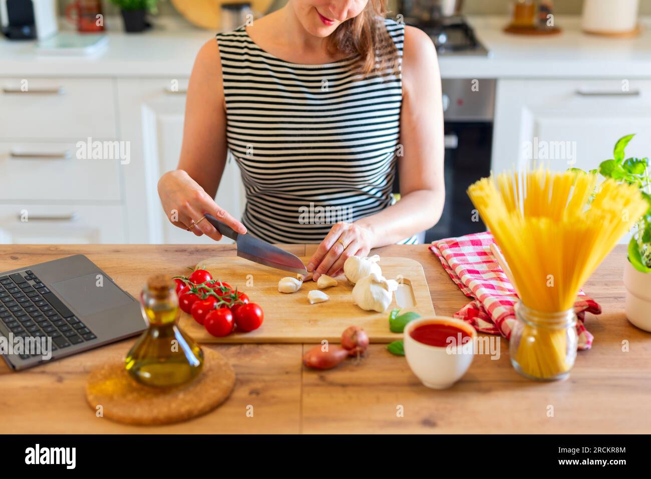 Eine junge, wunderschöne hispanische Frau, die italienische Pasta zubereitet und sich das Online-Rezept auf einem Laptop in der Küche ansieht Stockfoto