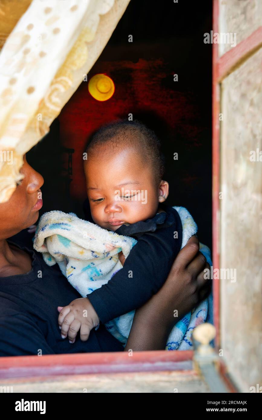 Die junge afrikanische Mutter hält ihr Baby am Fenster Stockfoto