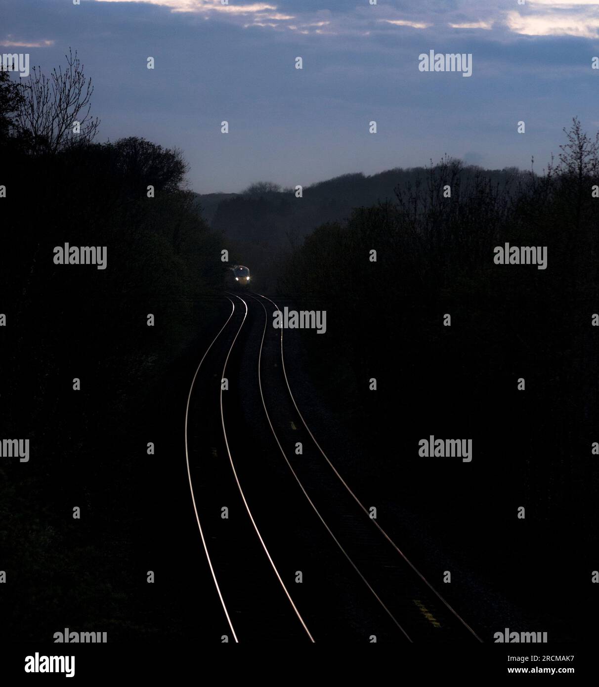 Bahnlinie mit einem Fernzug nähert sich nach Sonnenuntergang an einer S-Kurve auf der Hauptlinie von Südwales, Wales, Großbritannien Stockfoto