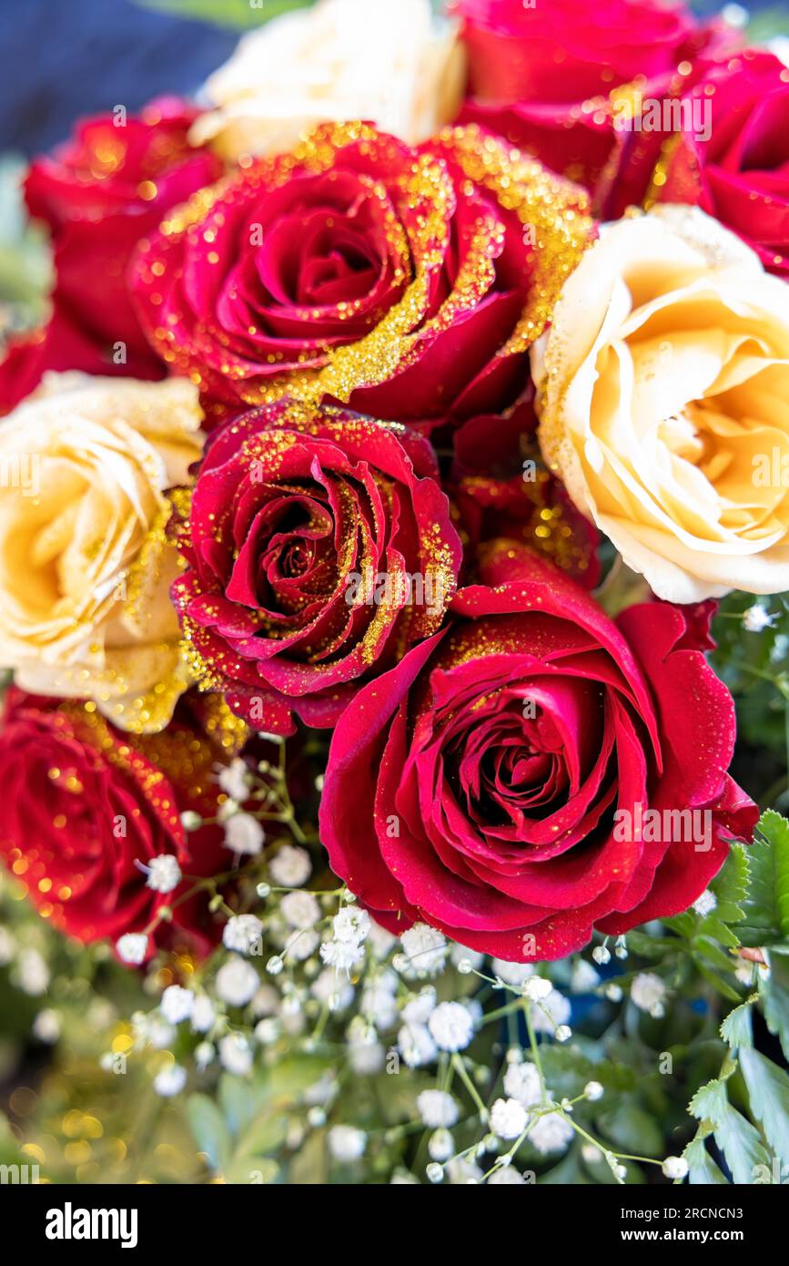 Blumenarrangements auf dem Tisch, Strauß aus roten und weißen Rosen mit goldenem Glitzer. Stockfoto