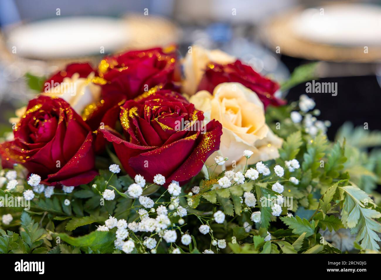 Blumenarrangements auf dem Tisch, Strauß aus roten und weißen Rosen mit goldenem Glitzer. Stockfoto