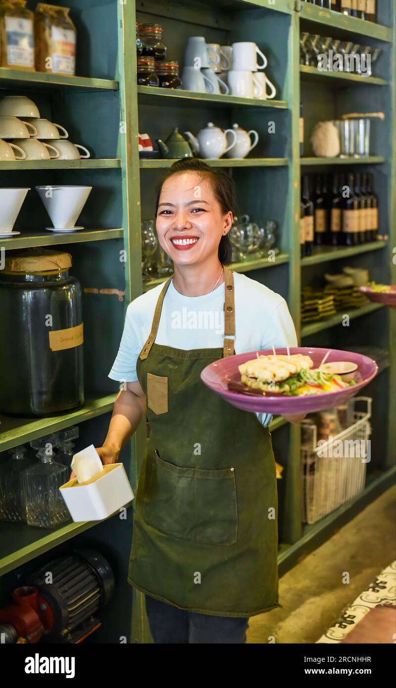 Vietnamesische Kellnerin, die belgische Waffeln mit Salat in einem Café serviert Stockfoto