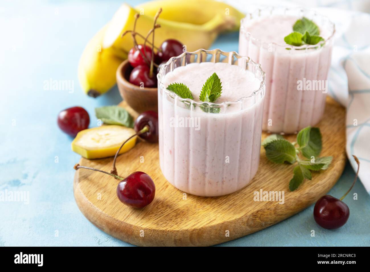 Frische Smoothies der Saison. Smoothies mit süßer Kirsche und Banane mit Joghurt auf Holzbrett auf Steinhintergrund. Speicherplatz kopieren. Stockfoto