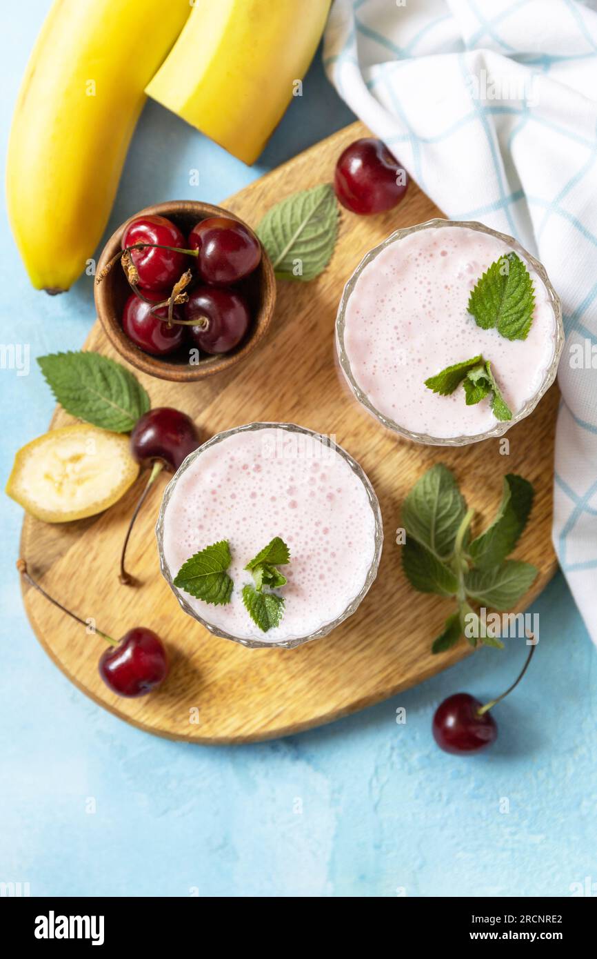 Smoothies mit süßer Kirsche und Banane mit Joghurt auf Holzbrett auf Steinhintergrund. Frische Smoothies der Saison. Blick von oben. Speicherplatz kopieren. Stockfoto