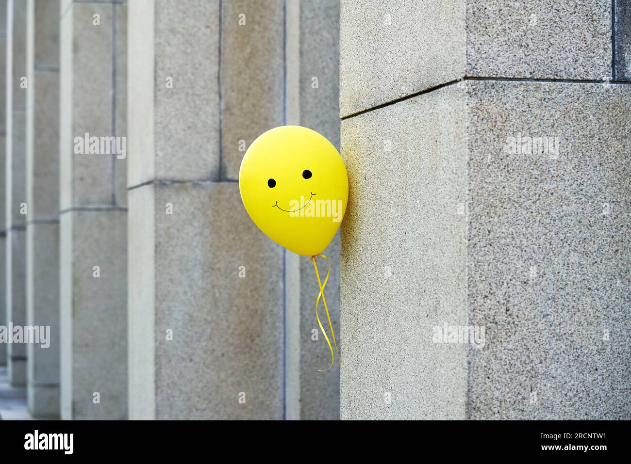 Gelber Ballon mit einem lächelnden Gesicht, das hinter die graue Wand blickt Stockfoto