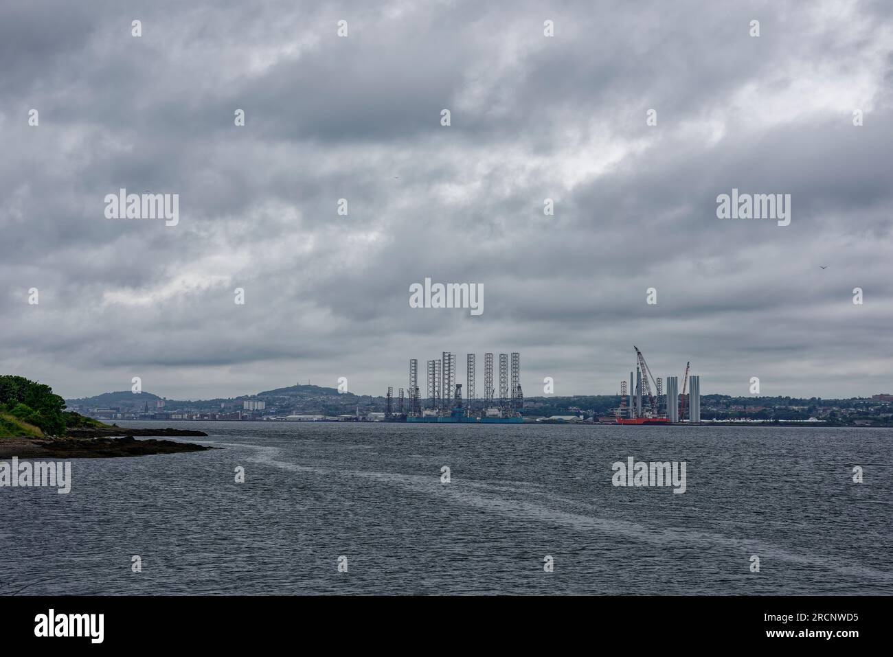 Der Blick auf den Hafen von Dundee von Tayport auf der anderen Seite der Tay-Mündung an einem dunklen Regentag im Juli mit Bohrinseln am Hafen. Stockfoto