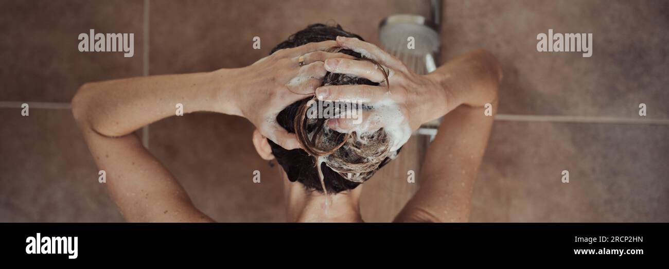 Blick von hinten auf eine Frau, die ihr Haar mit schäumendem Shampoo wäscht und in der Dusche im Badezimmer steht. Weitwinkelbild. Stockfoto