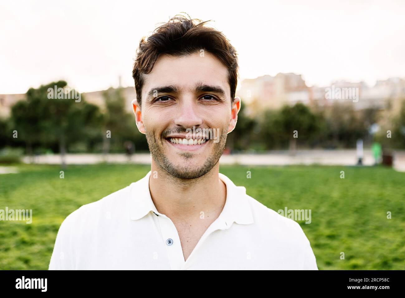 Außenporträt eines jungen, lächelnden, gutaussehenden Mannes, der in den Stadtpark schaut. Stockfoto
