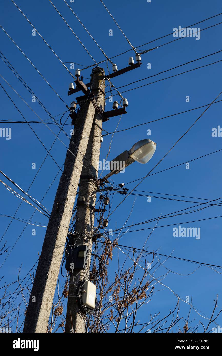 Elektrische Kabel hängen an einem Stab mit einer Lampe, die von unten auf einem Hintergrund mit blauem Himmel fotografiert wurde. Stockfoto