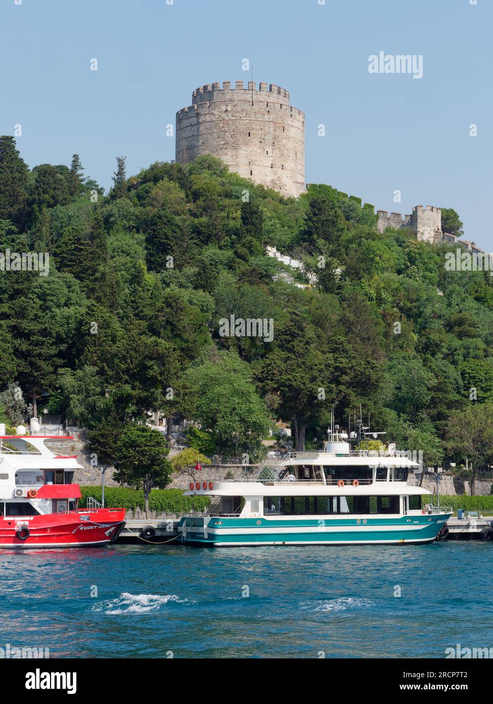 Festung Rumeli umgeben von Bäumen auf einem Hügel am Ufer des Bosporus mit Passagierfähren, Istanbul, Türkei Stockfoto