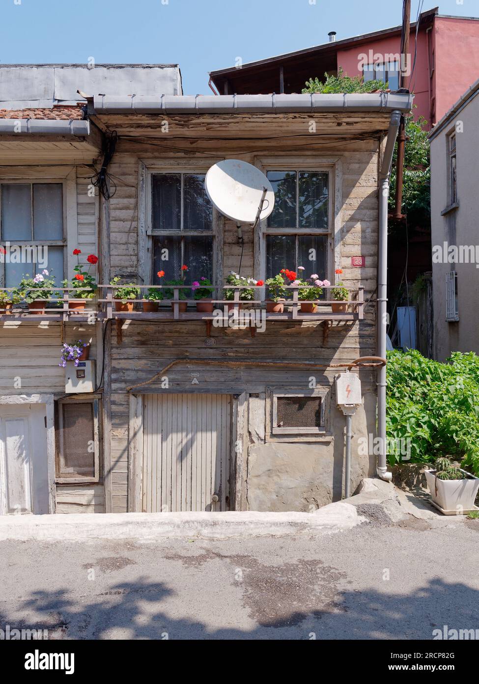 Heruntergekommenes, aber malerisches Haus in Anadolu mit einem hölzernen Fenstervorsprung voller Blumentöpfe und einer Satellitenschüssel darüber. Istanbul, Türkei Stockfoto