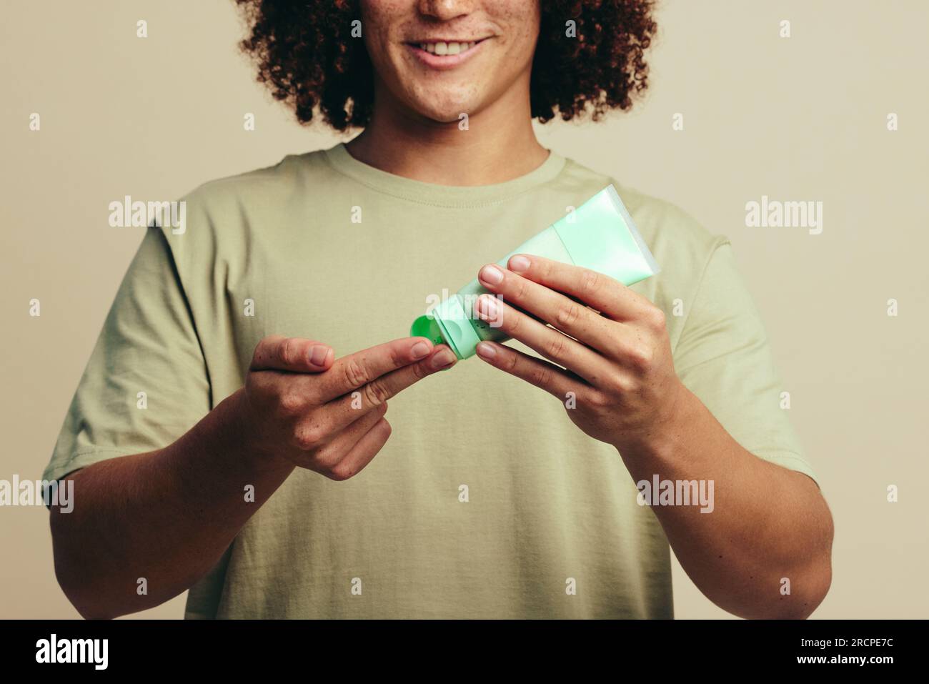 Glücklicher junger Mann, der sich eine Gesichtsmaskencreme auf die Finger legt, bevor er sie während seiner Hautpflege auf sein Gesicht aufträgt. Ein Mann, der sich mit einem um seine Haut kümmert Stockfoto