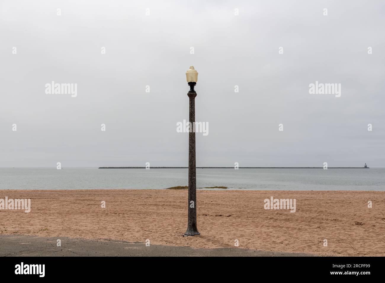 Panoramablick über den Strand des Lighthouse Point Park in New Haven, CT, USA, mit einer einzigen Straßenlaterne und Wellenbrecher in der Ferne mit historischem 1877 Building S. Stockfoto