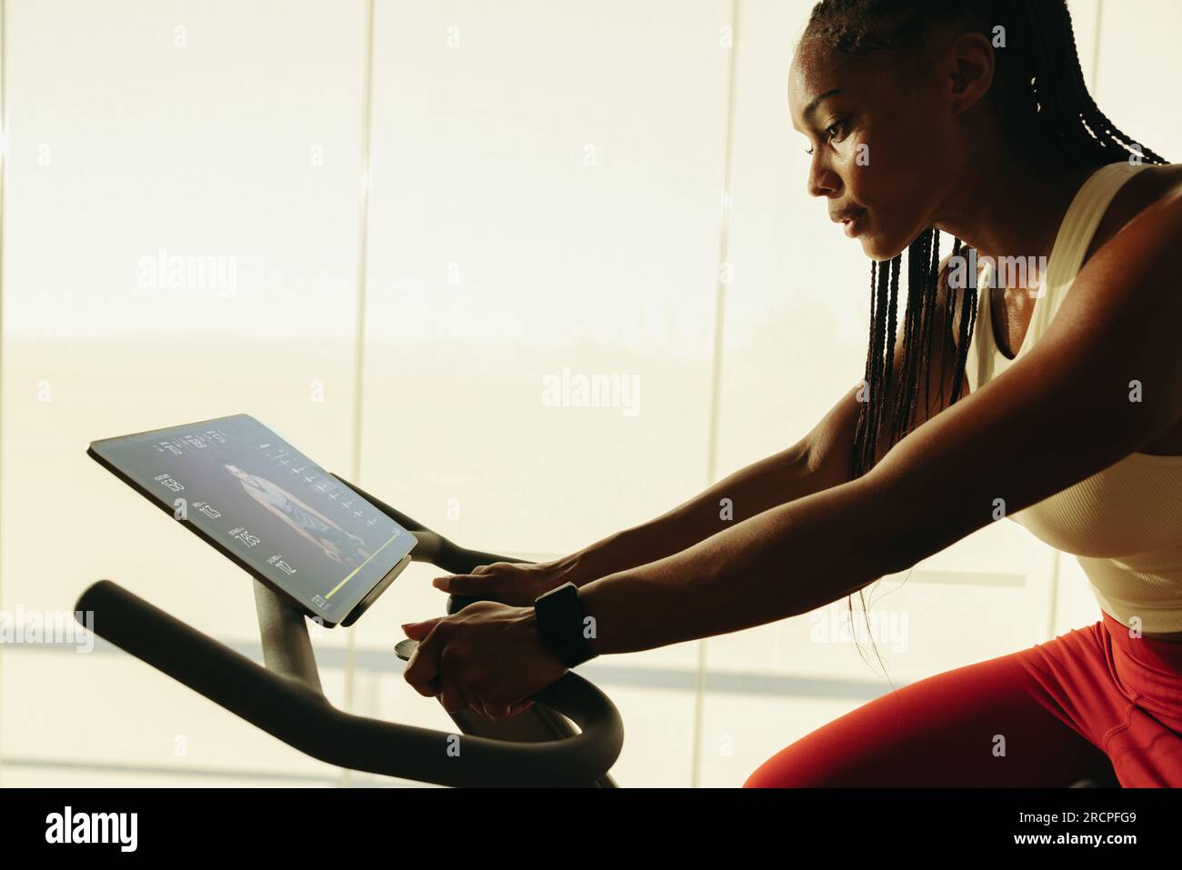 Eine afroamerikanische Frau, die eine Fitness-App verwendet, um ihr Heimtrainer-Workout zu Hause zu leiten. Junge schwarze Frau, die die Vorteile intelligenter Fitnessgeräte nutzt Stockfoto