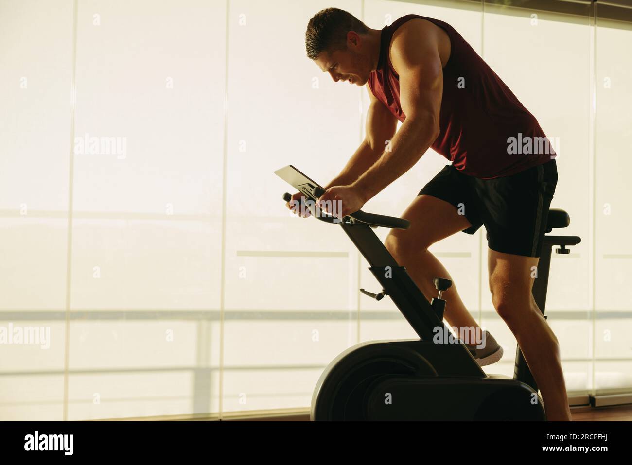 Junger weißer Mann, der sich auf seinem hochmodernen Fitness-Fahrrad neue Grenzen setzt und die neueste Fitness-Technologie nutzt, um seine Gesundheit zu erreichen Stockfoto