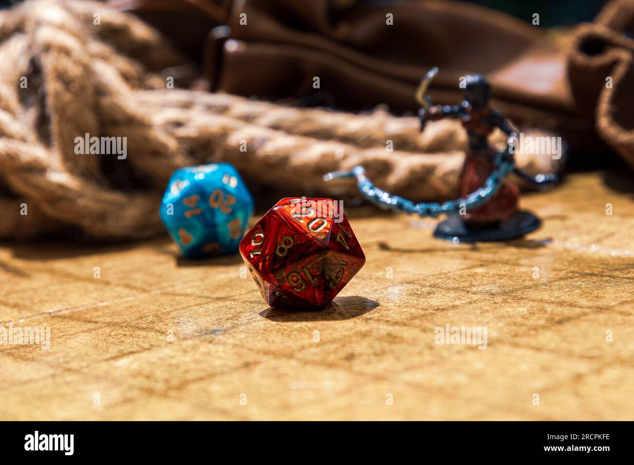 Aufnahme einer roten D20 aus einem tiefen Winkel auf einem Schlachtfeld, umgeben von einer blauen D20, Mini-Gaming, Seil und Münztasche Stockfoto